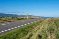 a paved road leading to the ocean on a sunny day and a hill behind it