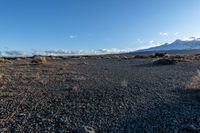 a person holding an electronic device in their hand on rocky ground next to snow capped mountains