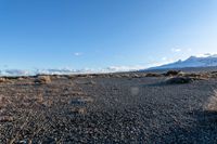 a person holding an electronic device in their hand on rocky ground next to snow capped mountains