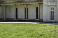 a tall white building with pillars and windows on the second floor has a lawn with a dog laying in front of it