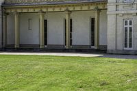 a tall white building with pillars and windows on the second floor has a lawn with a dog laying in front of it