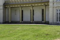 a tall white building with pillars and windows on the second floor has a lawn with a dog laying in front of it