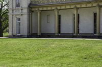 a tall white building with pillars and windows on the second floor has a lawn with a dog laying in front of it