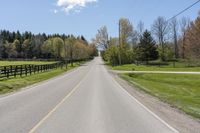 a empty country road with some trees in the distance and a fence behind it,