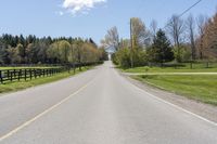 a empty country road with some trees in the distance and a fence behind it,