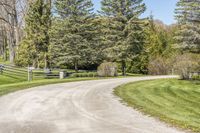 an empty rural road with a large gated gate in the distance between trees and a path lined with greenery