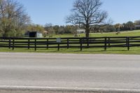 a horse is in the pasture by the road and fenced off by a bench