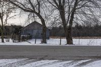 a barn is sitting behind some bare trees on a wintery day - like scene