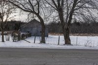 a barn is sitting behind some bare trees on a wintery day - like scene