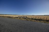 a wide empty roadway and gate by the side of a dirt road with grass around it