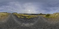 the photo has a fish eye lens of a rural road in australia looking across a muddy dirt road to a hill