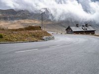 a small old cabin on the side of the road on a mountain slope with fog and clouds