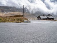 a small old cabin on the side of the road on a mountain slope with fog and clouds