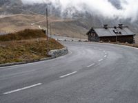 a small old cabin on the side of the road on a mountain slope with fog and clouds