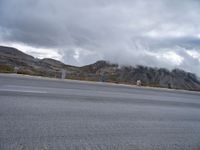 a person riding a motorbike down a deserted street below a mountain range filled with cloud