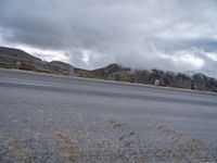 a person riding a motorbike down a deserted street below a mountain range filled with cloud