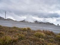 clouds hovering over mountains near road on cloudy day on highway below, near grassy area with a fire hydrant