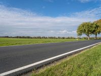 a road in the middle of green grass with trees and blue sky behind it near the roadway