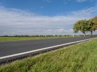 a road in the middle of green grass with trees and blue sky behind it near the roadway