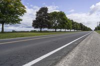 a country road with two lanes and one tree line down it's left side