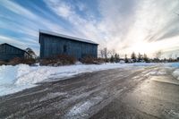 a road in front of some barn and buildings in the snow during the day time