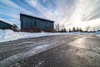 a road in front of some barn and buildings in the snow during the day time