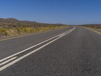 a lone road runs through a desert area and is bordered by a clear sky and hills