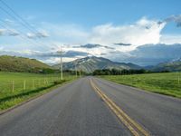 a lone country road is in the countryside area with mountains on both sides and barbed fence between the two sides