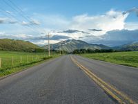 a lone country road is in the countryside area with mountains on both sides and barbed fence between the two sides