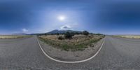 a fisheye lens shot of a rural road and mountains in the background and a partly cloudy sky