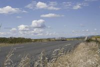 a lone highway with a truck parked on the side near it and clouds in the sky
