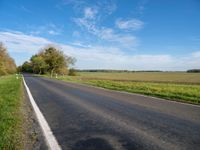 the road goes through a wide open space in the countryside area with green grass and trees