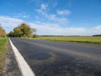 the road goes through a wide open space in the countryside area with green grass and trees