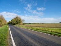 the road goes through a wide open space in the countryside area with green grass and trees