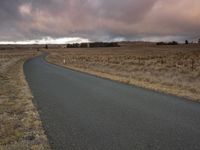 a road in a dry grassy field under stormy skies as seen from a distance with no vehicles on it