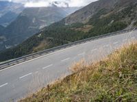 a man rides his motorcycle on a winding road above the mountains in italy on a cloudy day