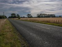 a lone road along a rural field under clouds in the country side way view of a motorcycle