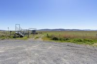 a fenced area with a gate on the edge and mountains in the distance on a clear day