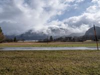 a grassy field with an empty road going through it and some mountains in the distance