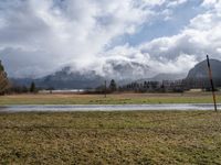 a grassy field with an empty road going through it and some mountains in the distance