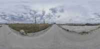 a road filled with dirt and lots of grass under a cloudy sky over farmland and dirt road