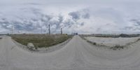 a road filled with dirt and lots of grass under a cloudy sky over farmland and dirt road