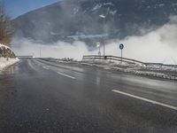 a snowy mountain sits above a empty road with signs on either side of it, near a large highway