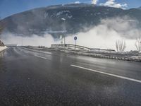 a snowy mountain sits above a empty road with signs on either side of it, near a large highway