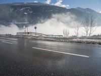 a snowy mountain sits above a empty road with signs on either side of it, near a large highway