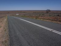 a lonely open country road with no traffic on it's sides, with dead grass on the ground and two white stripes in middle of each lane