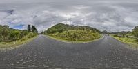 a wide open road stretches out into the sky near grassy hills and trees on both sides