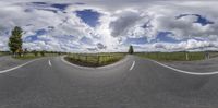 an empty road that has several different sides on it and clouds and blue sky behind