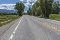 a road going down towards a field and mountain range with trees on both sides of the roadway