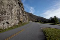 the road in front of a large rock wall is empty, with yellow lines on it